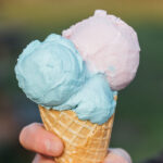Close up of hand holding waffle cone with pink and blue scoops of ice cream together.