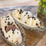 Ice Cream Banana Sundae dishes topped with chocolate sprinkles next too jug fresh flowers
