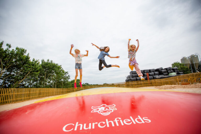 3 girls leaping in mid air on giant bouncer with Churchfields logo in foreground.