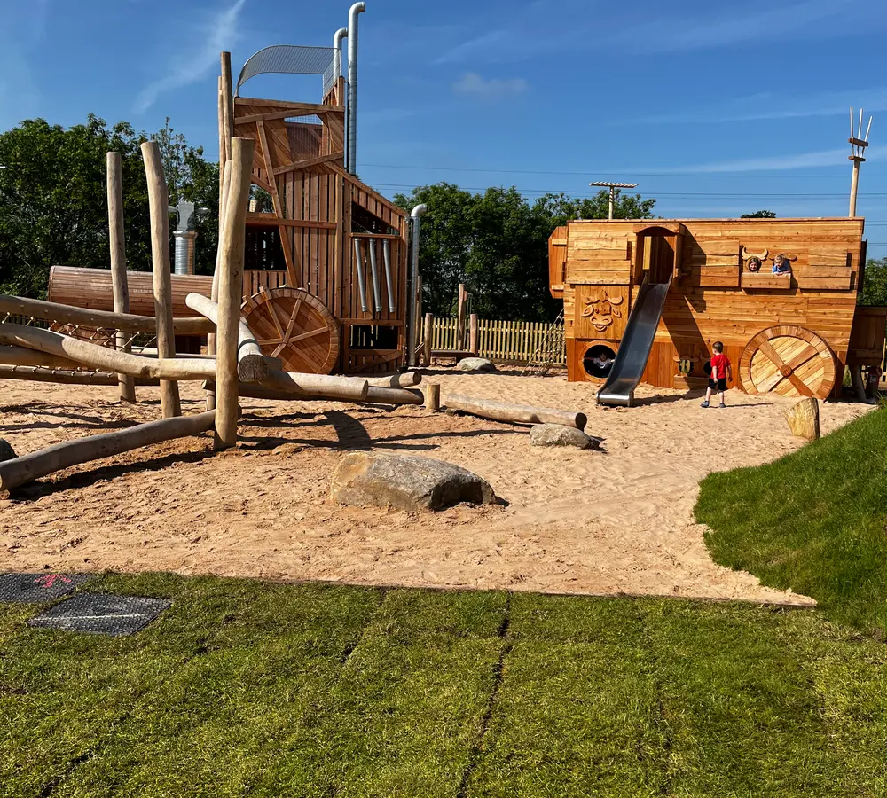 View of tractor and trailer adventure playground elements on sunny day with grass in foreground
