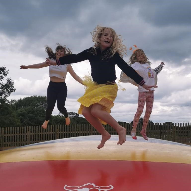 3 Girls wearing bright clothes in mid air, bouncing on giant bouncer with black cloud behind them