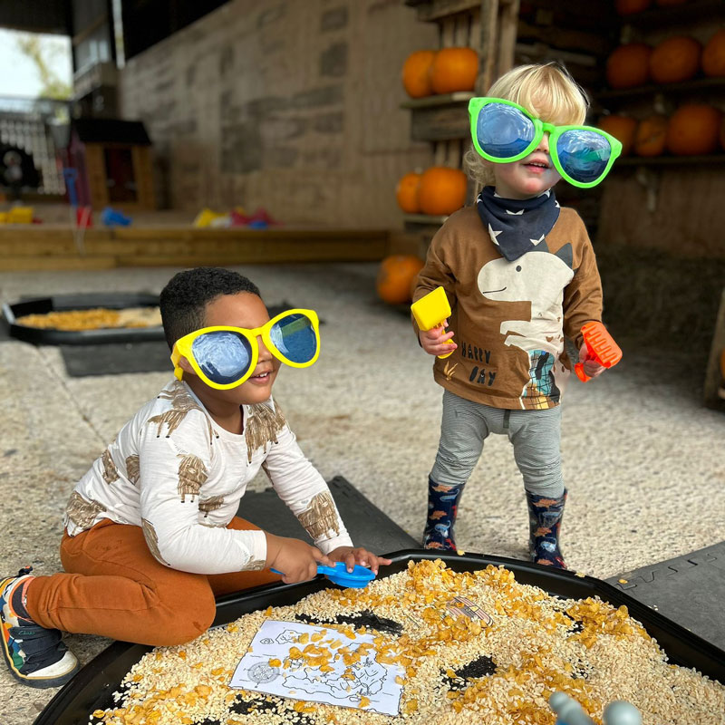 Preschool children with oversized sun glasses playing in messy play tray with small spades